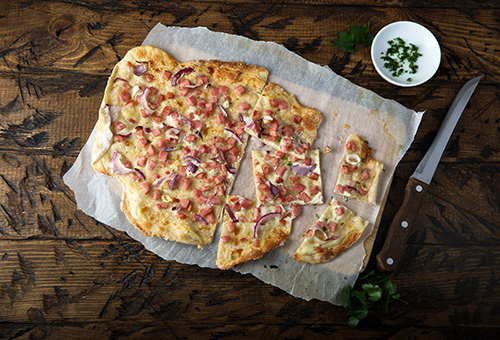 Elsässer Flammkuchen mit Zwiebel & Speck auf einem Holzbrett