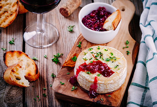 Gebackener Camembert mit Preiselbeeren auf einem Holzbrett angerichtet und mit Thymian dekoriert