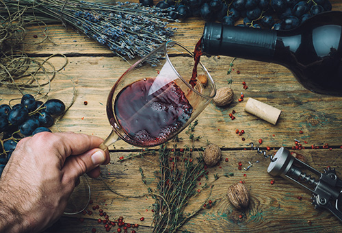 Rotwein wird vor einem rustikalen Holz-Hintergrund in ein Glas ausgeschenkt