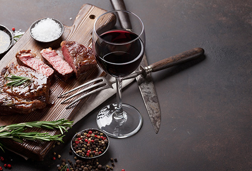 Gegrilltest, aufgeschnittenes Steak auf Holzbrett serviert, daneben ein Glas Rotwein