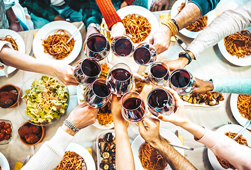 Zehr Personen, die mit Rotwein über einem Tisch mit Tellern mit Pasta anstoßen