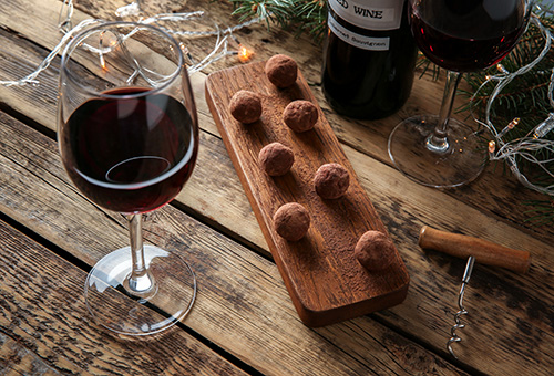 Rotwein, Schokoladenpralinen und Weihnachtsdekoration auf einem Holztisch