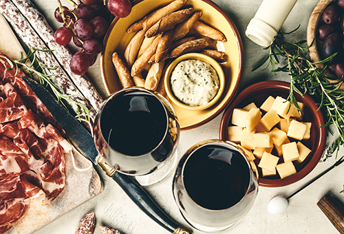 Schinken, Salami, Oliven, Käse und Brotsticks auf einem Tisch mit zwei Gläsern Rotwein