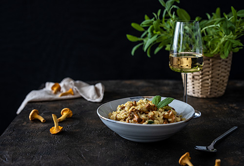 Ein Teller mit Pilzrisotto auf einem Tisch mit einem Glas Weißwein