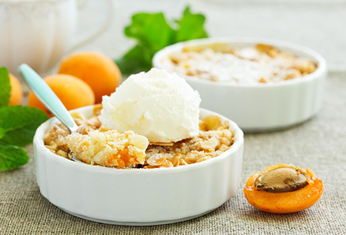 Aprikosencrumble in zwei kleinen Auflaufförmchen mit einer Kugel Vanilleeeis