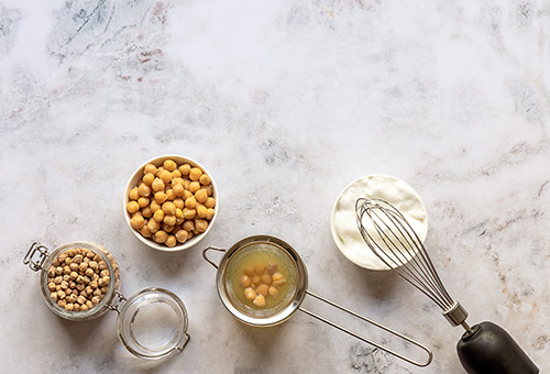 Getrocknete Kichererbsen, gekochte Kichererbsen, Aquafaba und veganer Eischnee in Glasschüsseln