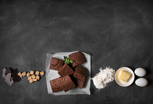 Brownie-Zutaten: Schokolade, Zucker, Mehr, Butter, Eier auf einem dunklen Hintergrund