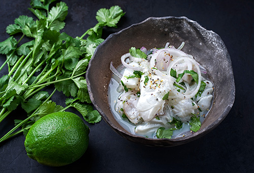 Ceviche aus weißem Fisch mit Zwiebeln, Koriander und Limetten als Deko daneben