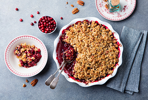 Cranberrycrumble in einer weißen Auflaufform, daneben eine Schüssel mit Cranberries