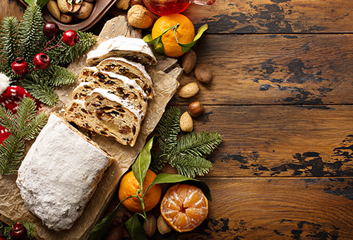 Angeschnittener Marzipanstollen auf einem Holzbrett, Mandarinen und Tannenzweige als Dekoration