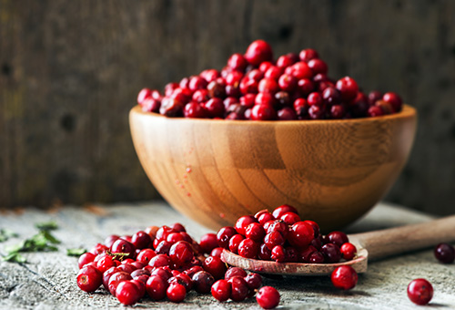 Reife, geerntete Preiselbeeren in einer Holzschüssel und davor auf einem großen Holzlöffel