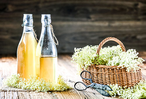 Sirup aus Holunderblüten mit einem Holzkorb mit Holunderblüten