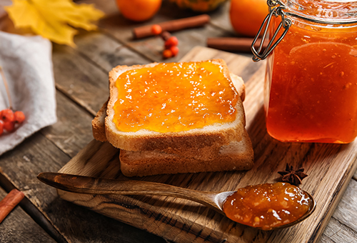 Orangenmarmelade auf einer Scheibe Toast angerichtet auf einem Holzbrett. 