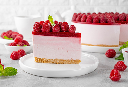 Ein Stück Himbeer Johgurt Torte auf einem Teller angerichtet und dekoriert mit frischen Himbeeren und Minze