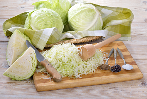 Weißkohl gehobelt auf einem Holzbrett mit Gewürzen zur Zubereitung von Sauerkraut.