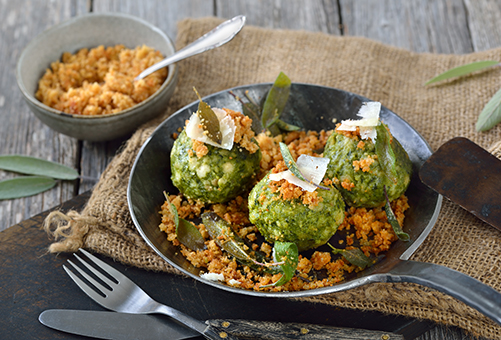 Drei vegetarische Spinatknödel in einer Gusspfanne angerichtet mit Röstzwiebeln in einer Gusspfanne.