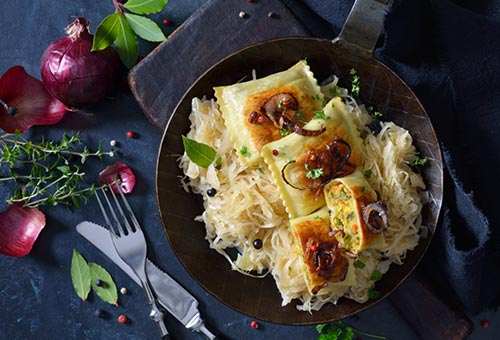 angebratene Maultaschen auf Zwiebeln in einer Gusspfanne angerichtet