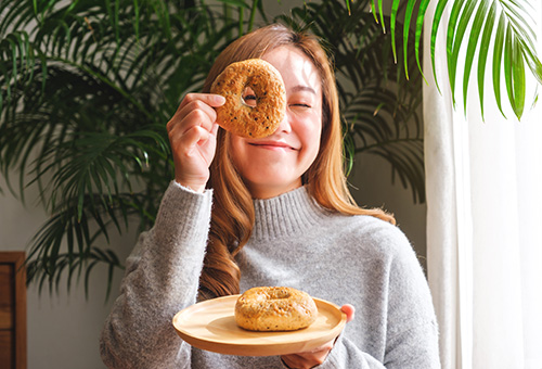 Frau hält Bagel vor ihrem Gesicht