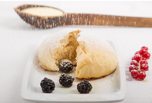 Geteilte Dampfnudel mit Brombeeren und Puderzucker angerichtet